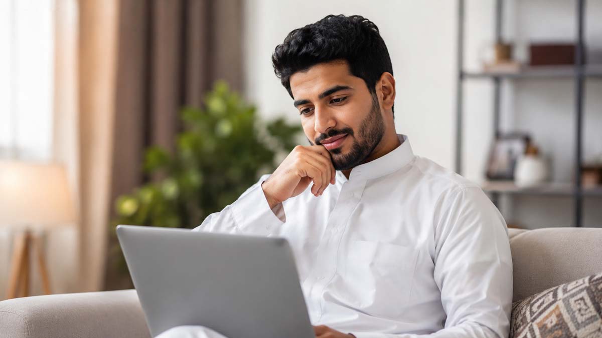 رجل شاب يجلس في غرفة معيشة حديثة ويتأمل شاشة حاسوبه المحمول بهدوء أثناء استكشاف اختبارات الشخصية